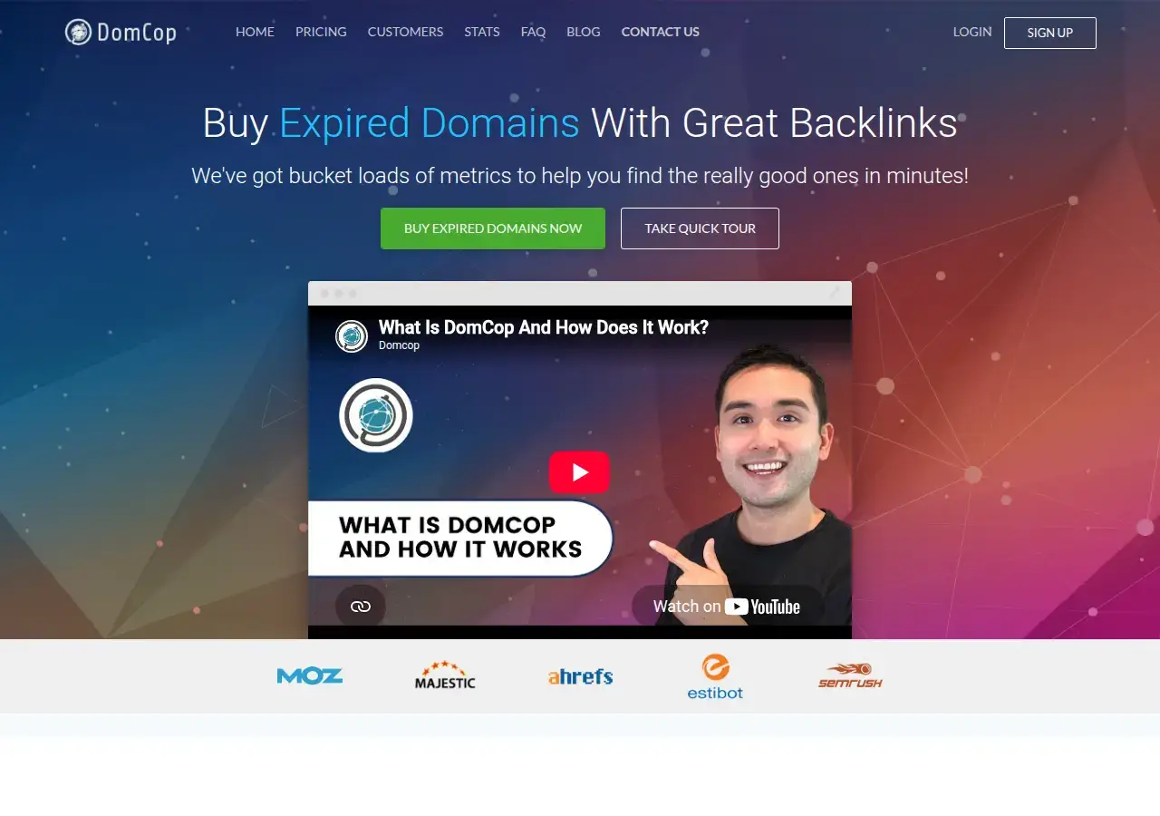 DomCop homepage with the headline Buy Expired Domains With Great Backlinks, top navigation, an intro video and logos of Moz, Majestic, Ahrefs, Estibot and Semrush